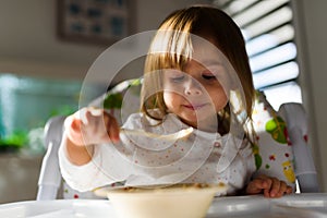 Two years old eats brakefast by herself with a spoon