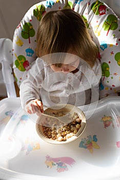 Two years old eats brakefast by herself with a spoon