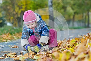 Two years old girl holding thermos flask cup hunkering at autumn foliage covering backdrop