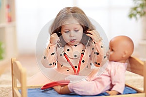 Two years old girl playing doctor with doll in the nursery