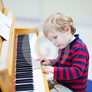 Two years old toddler boy playing piano, music schoool.