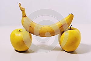 Two yellow apples and a banana on a white background