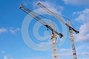 Two yellow construction cranes against blue sky with a few cloud
