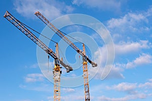 Two yellow construction cranes against blue sky with a few cloud