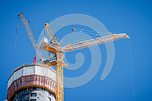 Two yellow cranes on top of a skyscraper under construction on a blue clear sky.