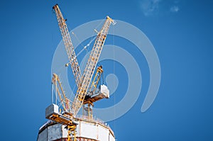 Two yellow cranes on top of a skyscraper under construction on a blue clear sky.