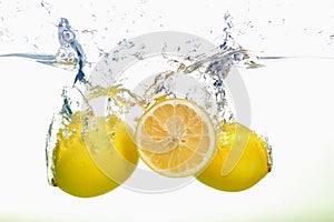 Two yellow lemons and lemon slice spash in water on white background
