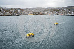Two yellow lifeboat driving back to AIDA Bella cruise ship, Port of Shetland Island in the Background, Scotland