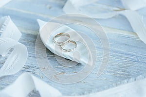 Two yellow and white gold wedding rings on a ceramic decorative white leaf and a blue wooden table, white decorative