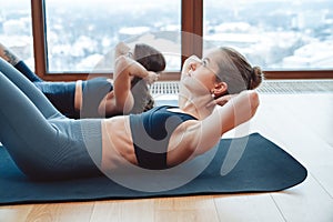 Two young active women with slim body doing press laying on mats on floor.