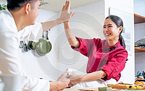 Two young adult Asian professional couple chefs wearing uniform, hat, happily smiling with confidence, happiness, giving high five