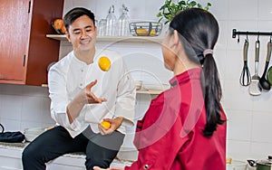 Two young adult Asian professional couple chefs wearing uniform, hat, happily smiling with confidence, standing, playing with fun