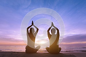 Two young adult doing a yoga training at the beach during sunset for meditation and healthy life