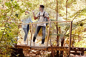 Two young adult friends hiking in a forest crossing a footbridge, full length