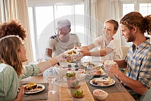 Two young adult women passing a dish across the dinner table during lunch with friends, close up