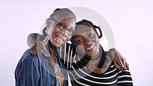 Two young african american women hugging and smiling at camera, happy, isolated over white background, black friends