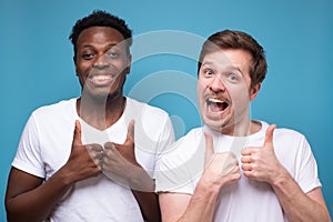 Two young african and caucasian men doing happy thumbs up gesture with hand approving expression