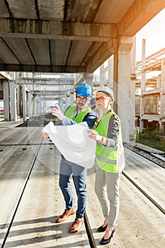 Two young architects visiting large construction site, looking at floor plans