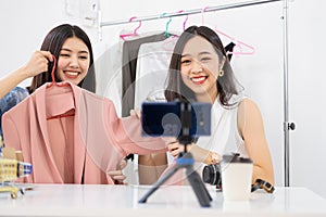 Two young asian attractive woman vloggers sitting in home present cloth dress online business shop online ideas concept.