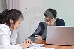 Two young Asian business people analyzing paper work or charts together in modern office. Team work business concept. Selective fo