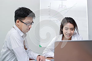 Two young Asian business people working with laptop together in modern office. Team work business concept. Selective focus and sha