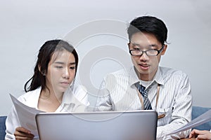 Two young Asian business people working with laptop together in modern office. Team work business concept. Selective focus and sha