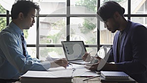 Two young asian businessmen in suits discussing financial market data in office Business team working