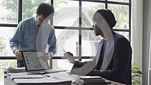 Two young asian businessmen in suits discussing financial market data in office Business team working