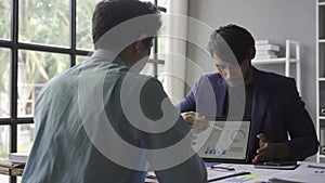 Two young asian businessmen in suits discussing financial market data in office Business team working