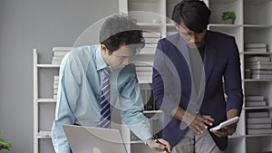 Two young asian businessmen in suits discussing financial market data in office Business team working