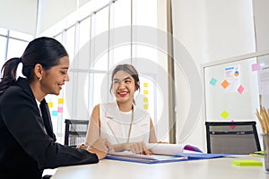 Two young Asian businesswoman in smart casuals read some documents, making plans together. Business people talking together with