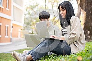 Two young Asian college students are discussing work and using their laptop at a campus park