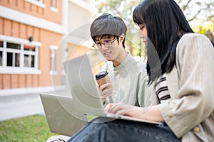 Two young Asian college students are discussing work and using their laptop at a campus park