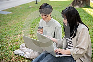 Two young Asian college students are discussing work and using their laptop at a campus park