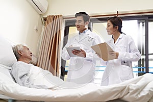Two young asian doctors talking old man at bedside