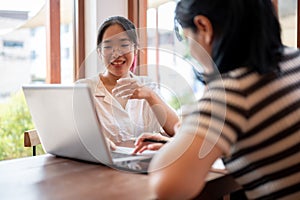Two young Asian female college students are working on a project together, meeting at a coffee shop