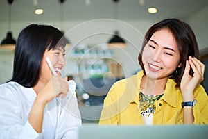 Two young Asian freelance working women chatting with each other smilingly in a modern coworking space photo