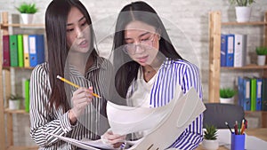 Two young asian girls office workers discuss documents close up