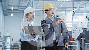 Two Young Asian Heavy Industry Engineers in Hard Hats Walking with Laptop Computer and Talking in a