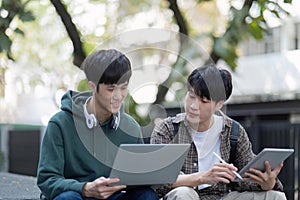 Two young Asian male college students discussing and working on their school project together