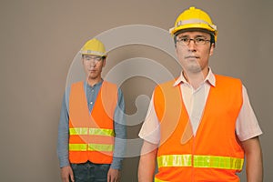 Two young Asian men construction worker together against gray background