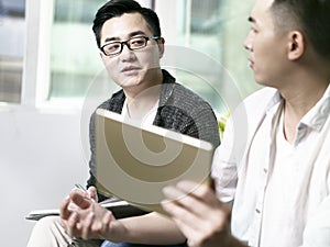 Two young asian men discussing business in office