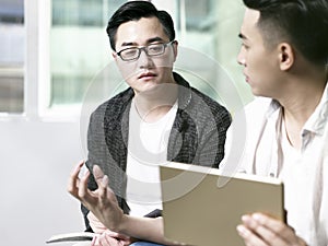 Two young asian men discussing business in office