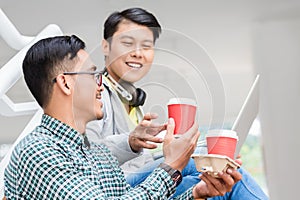 Two young Asian men using a laptop while relaxing during break