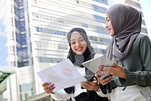 Two young Asian Muslim businesswomen stand together in a central business district