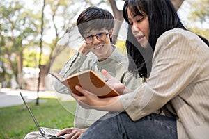 Two young Asian university students are preparing for an exam together in the university park