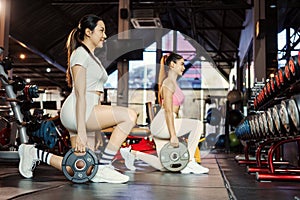 Two young asian woman doing exercises with heavy weights plates in gym