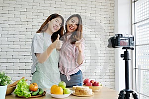 Two young asian woman food bloggers talking and thumb up while recording video, vlog concept, people, food and technology