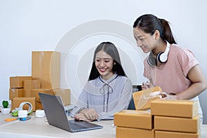 Two young Asian women chat with bright smiles to customers who shop online via laptop and confirm the order to close the deal