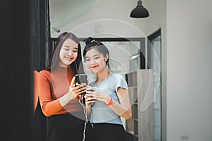 Two young asian women listening to music on couch in living room at home.